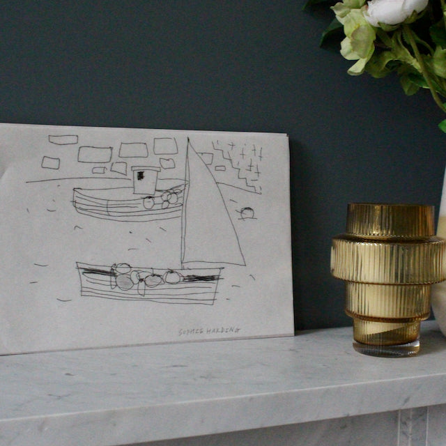 drawing by Sophie Harding of a sailing boat in a harbour it is resting on marble top next to a glass vase with some flowers 