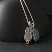 double silver pendant on a silver chain with one green stone and one small orange topaz it is by jeweller Carin Lindberg 