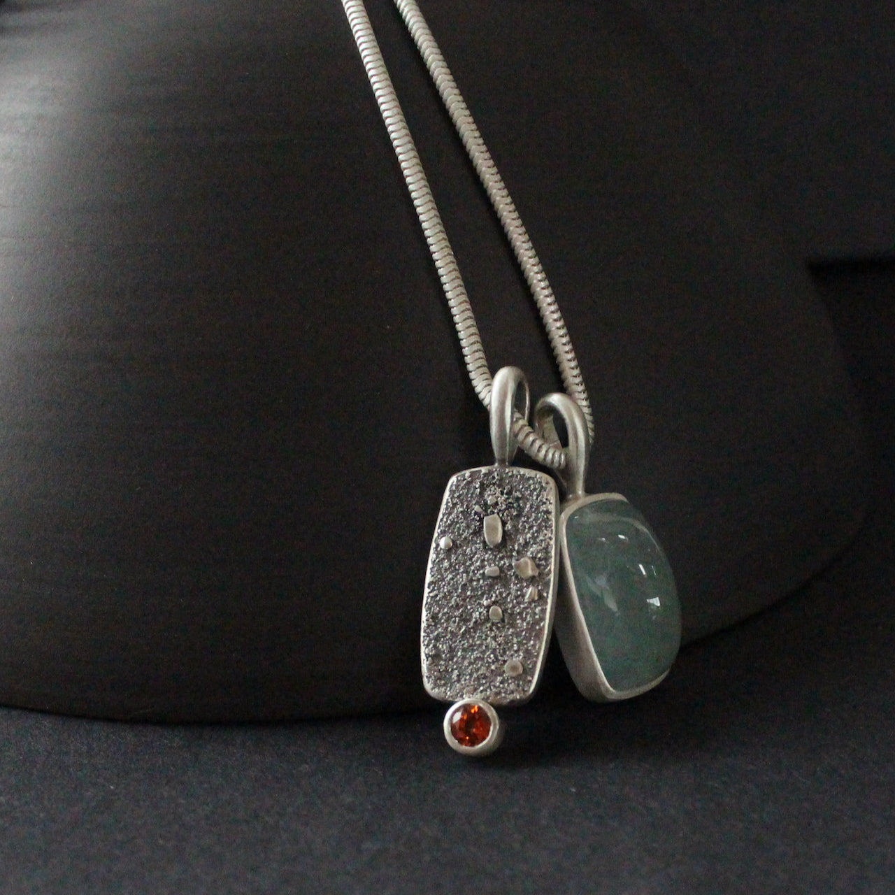 double silver pendant on a silver chain with one green stone and one small orange topaz it is by jeweller Carin Lindberg 