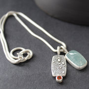 double silver pendant on a silver chain with one green stone and one small orange topaz it is by Cornwall based Swedish jeweller Carin Lindberg 