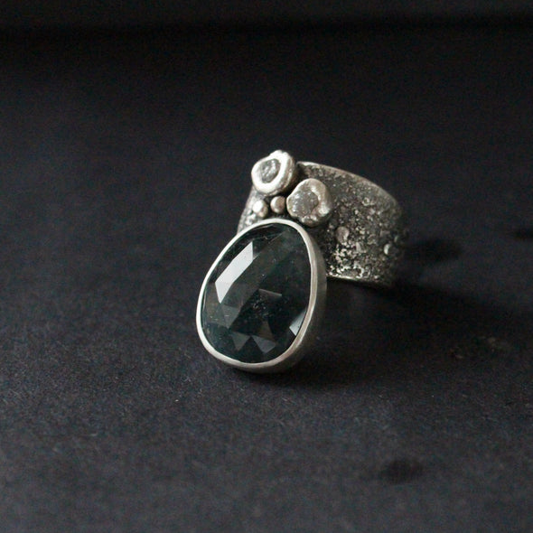 a textured and embellished silver  ring with a large dark blue green stone by jeweller Carin Lindberg