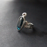 a textured silver  ring with a large dark blue green stone and smaller brown diamond by Swedish  jeweller Carin Lindberg who lives in Cornwall UK