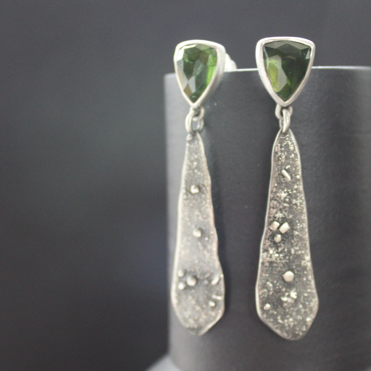 a pair of textured silver earrings with a dark green stone by jeweller Carin Lindberg