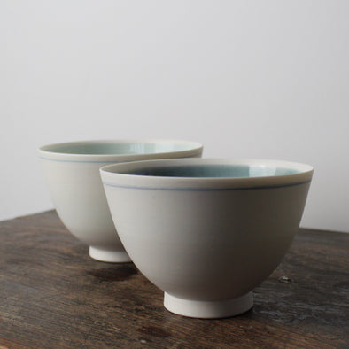 A pair of small white porcelain bowls one with pale turquoise and one with mid blue interior  by Kathryn Sherriff of By the Line Pottery, UK.