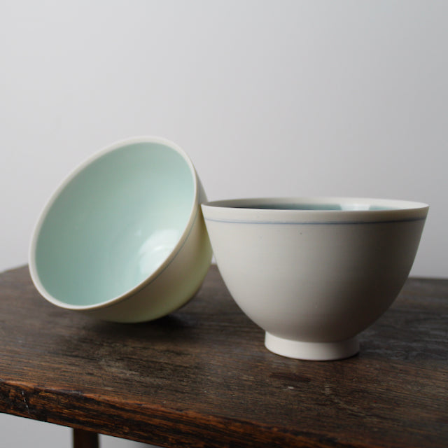 two small white porcelain bowls one with pale turquoise and one with mid blue interior  by Kathryn Sherriff of By the Line Pottery, England.