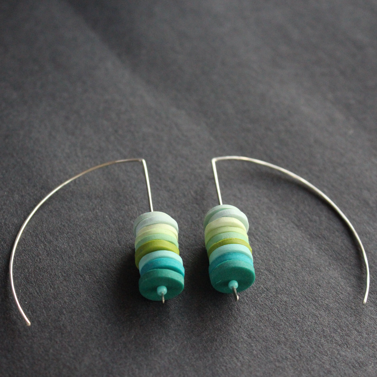 a pair of earrings made of small discs on top of each other in shades of blues and green by jewellery designer Clare Lloyd.