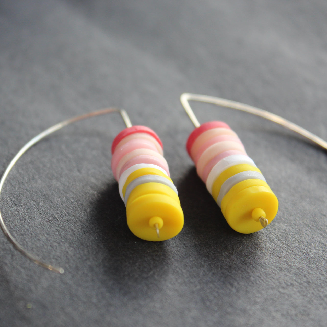 a pair of earrings made of small discs on top of each other in yellow and shades of pink by jewellery designer Clare Lloyd 