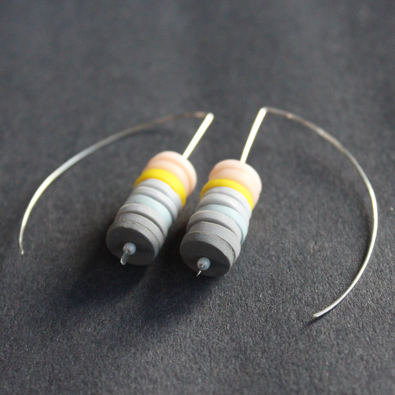 a pair of earrings made of small discs on top of each other in shades of grey and pink by jewellery designer Clare Lloyd 