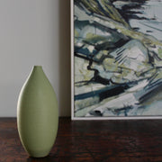 a spring Green oval vase by UK ceramic artist Lucy Burley next to the corner of a painting of the Cornish coast by Imogen Bone