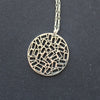 A round silver pendant on a chain, the centre is made up of cut out rectangles and small circles, on a silver chain