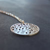 A round silver pendant on a chain, the centre is made up of cut out rectangles and small circles 