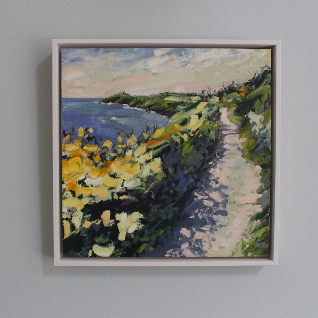 a framed painting by artist Jill Hudson of the coast path and looking towards Rame Head in south east Cornwall