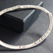 close up of a silver bangle with the words up we get to gather embossed on it by jeweller Lizzie Weir of Anatole Design.