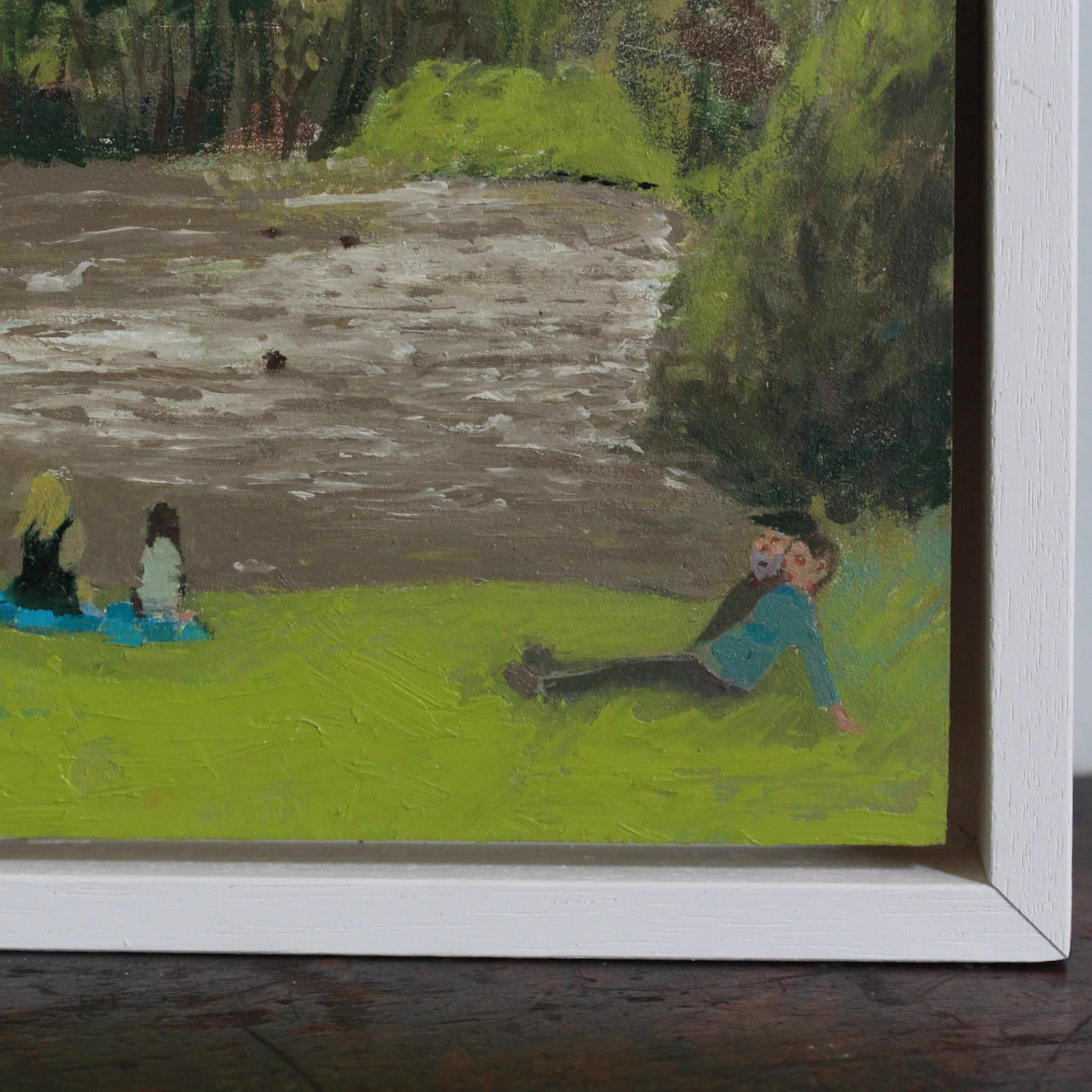 detail of a painting by Cornish artist Siobhan Purdy of people sitting on the grass in front of a lake.
