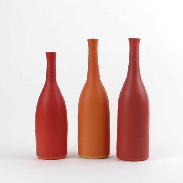 A trio of  Lucy Burley ceramic bottles in shades of red and orange sitting on a white background.