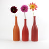 A trio of  Lucy Burley ceramic bottles in shades of red and orange each with a colourful flowers in it.