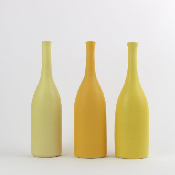 A trio of Lucy Burley ceramic bottles in shades of yellow  sitting on a white background