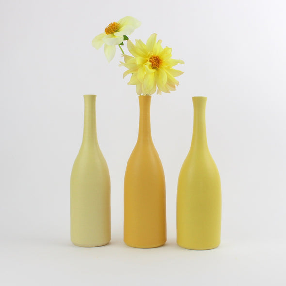 A trio of Lucy Burley ceramic bottles in shades of yellow the middle one has two yellow flower heads in it