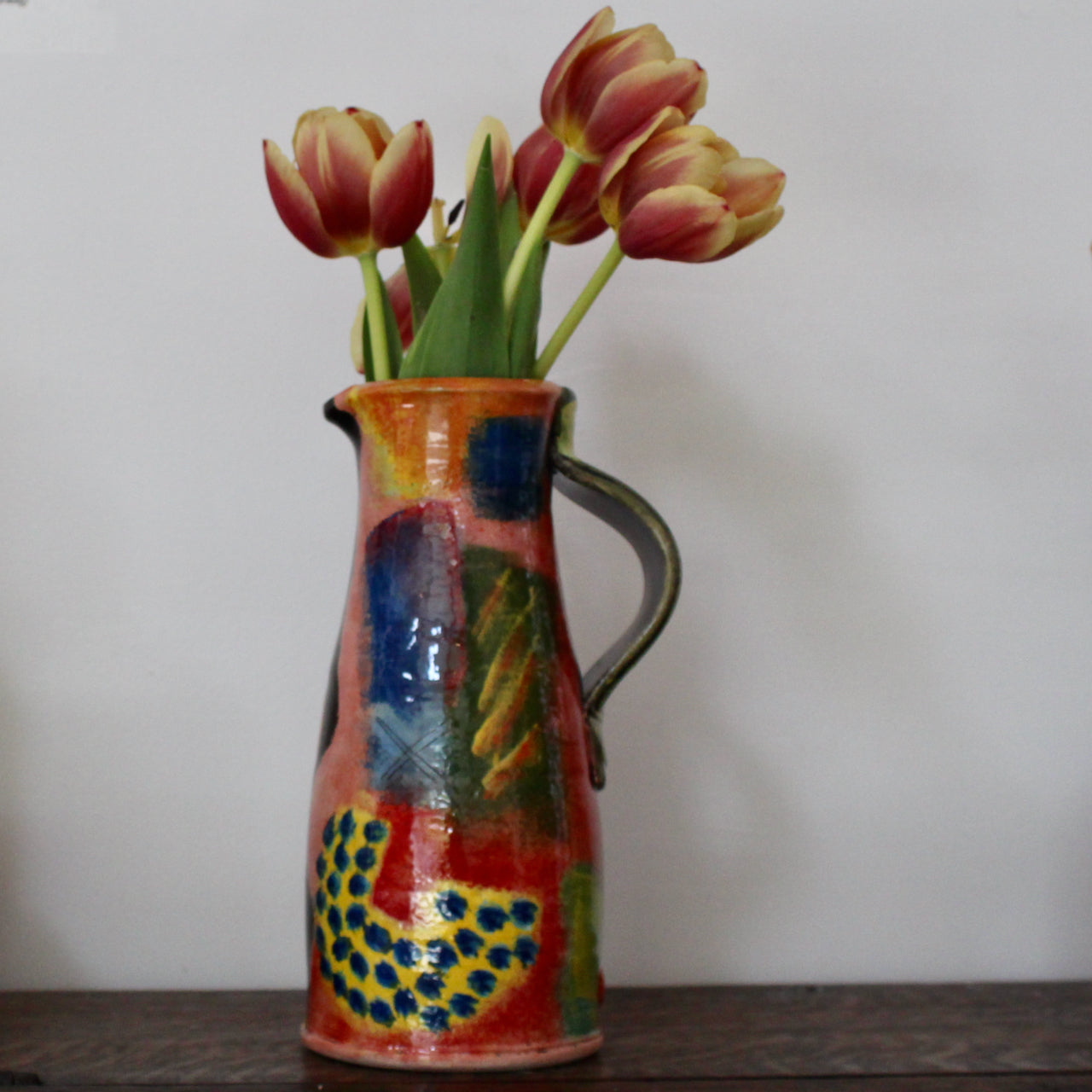 a multi-coloured ceramic jug by UK potter John Pollex it has a bunch of tulips 