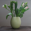 almond green curved vase with spring flowers in it by Lucy Burley on a wooden table