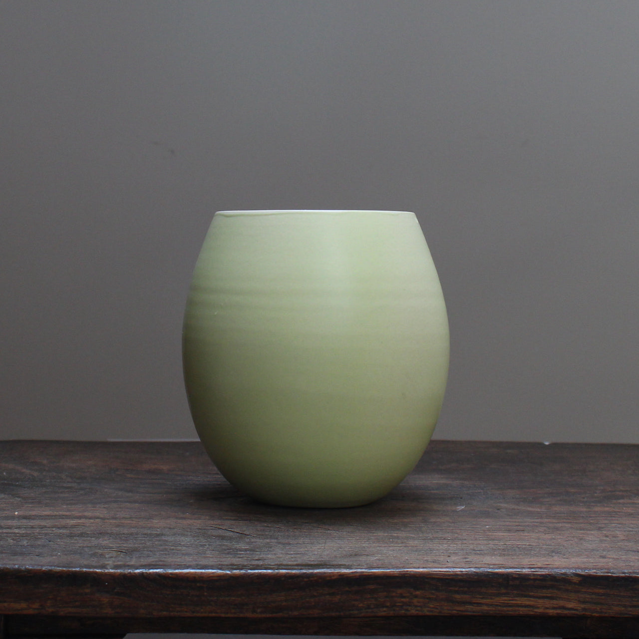 almond green curved vase by Lucy Burley on a wooden table