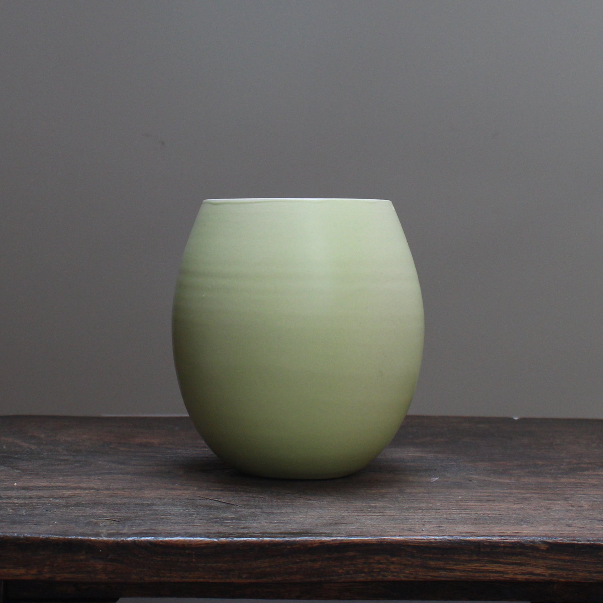 almond green curved vase by Lucy Burley on a wooden table