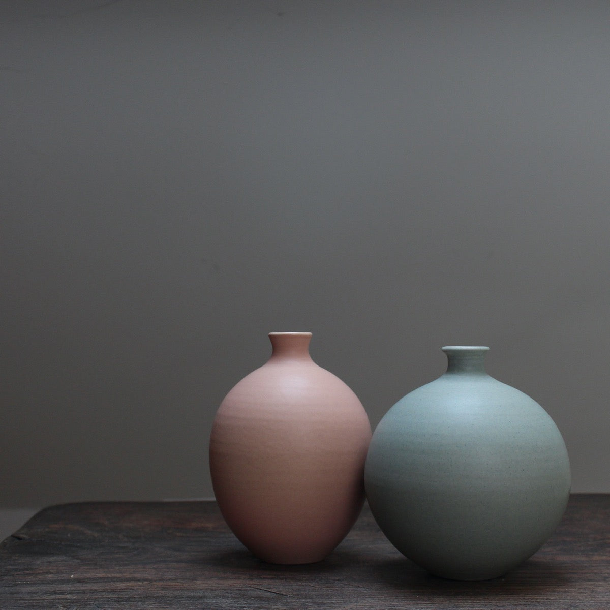 Two ceramic bottles on a wooden table - an oval shaped pale pink one and a round light green