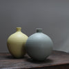 Two round ceramic bottles by Lucy Burley - one pale yellow and one pale green - on a wooden table