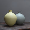 Two round ceramic bottles, one in pale yellow and one light sage on a wooden table at the Byre Gallery 