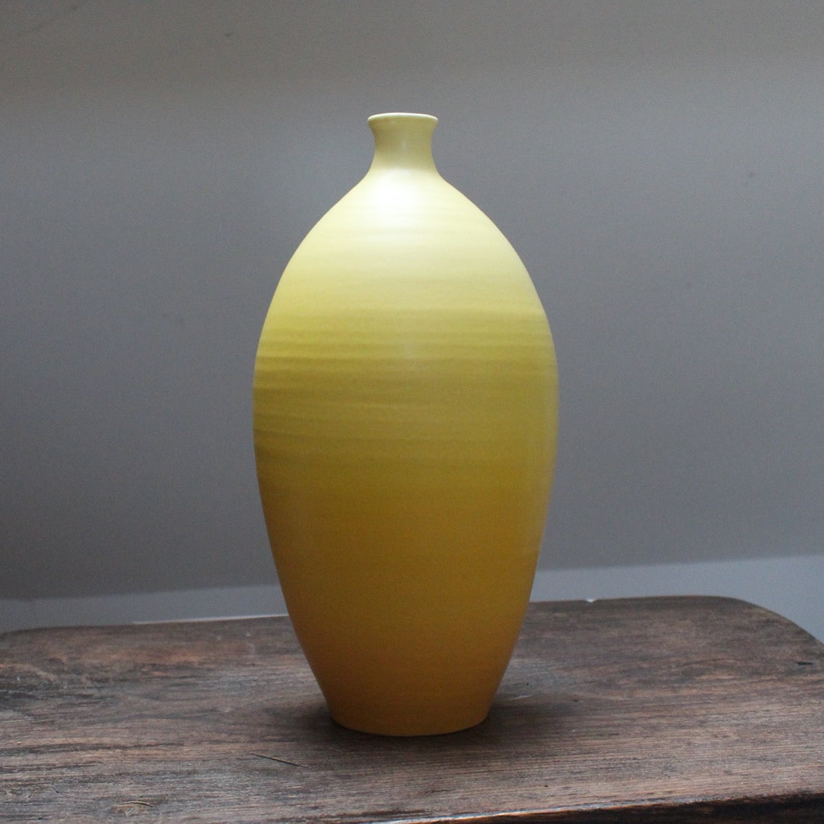Tall yellow curved bottle by Lucy Burley on a wooden table