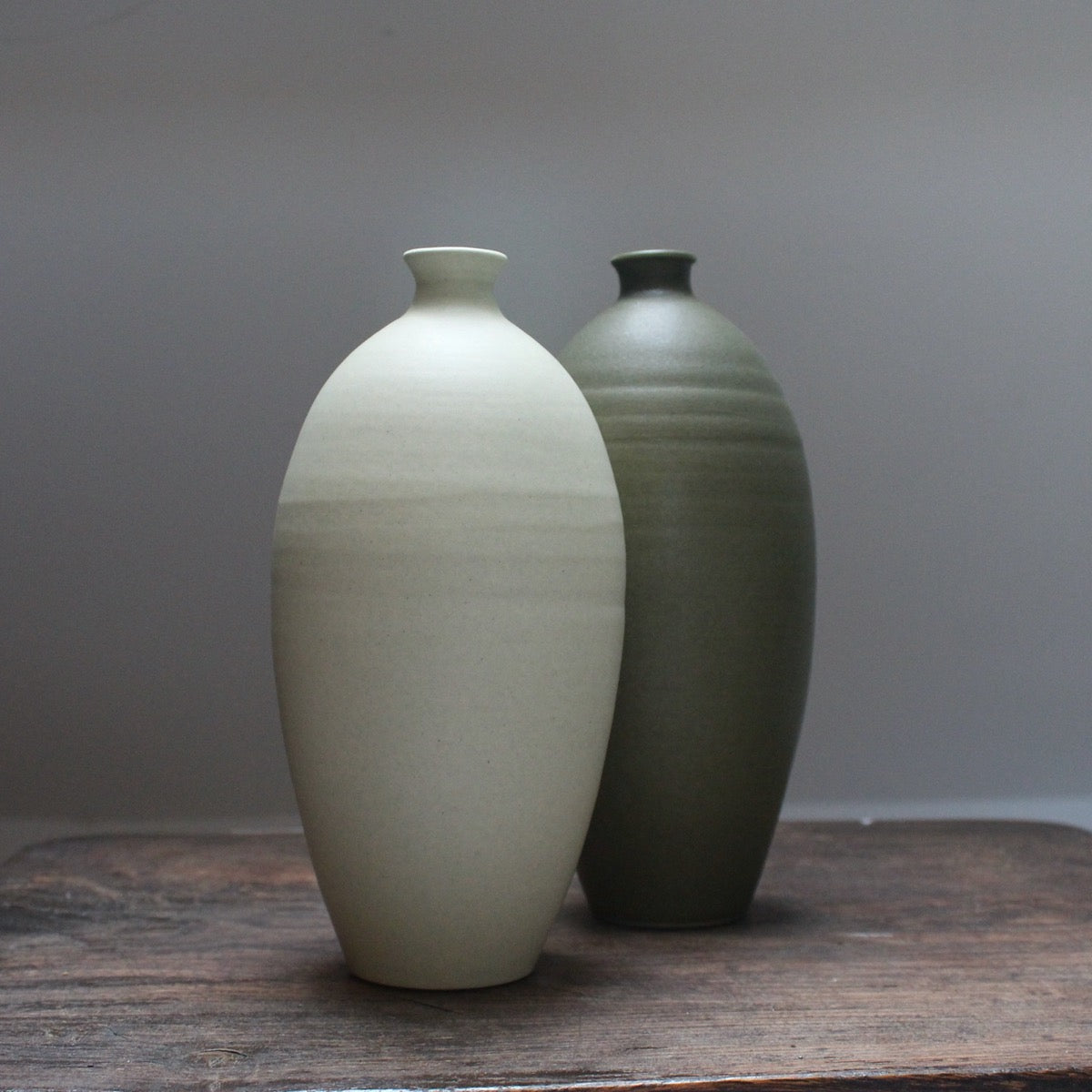 A pale green and a dark green ceramic bottle side by side on a wooden table 