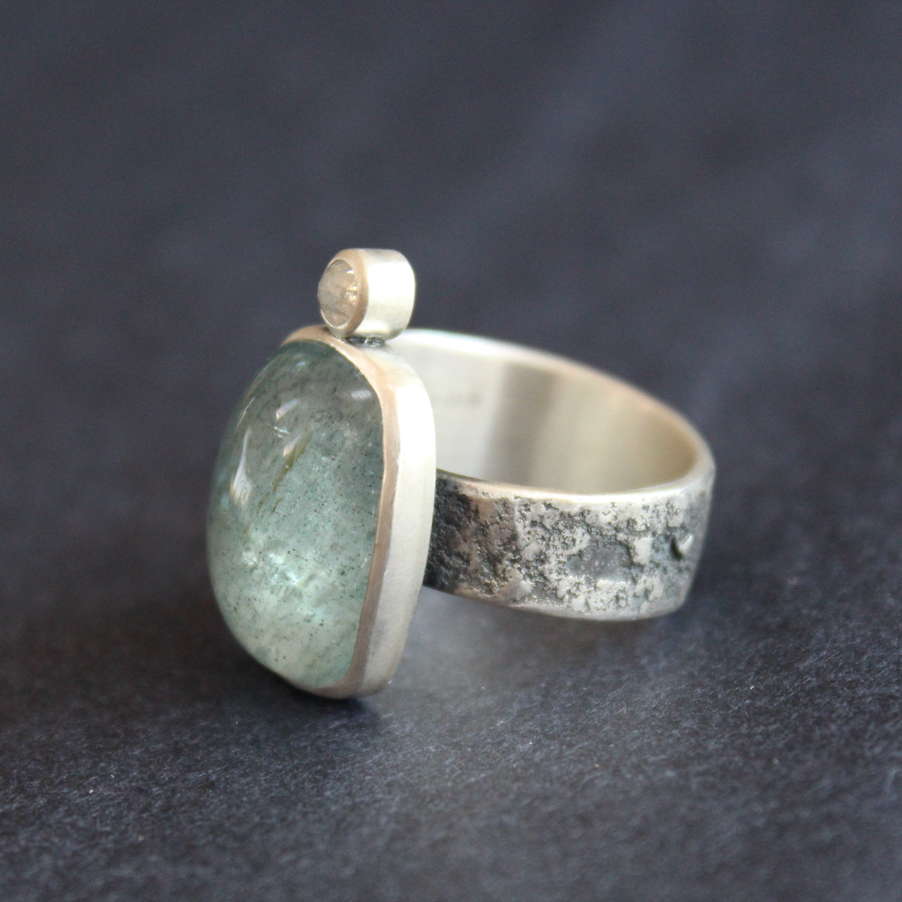 silver ring with a pale blue aquamarine stone and smaller diamond on a textured silver band by Cornwall jeweller Carin Lindberg