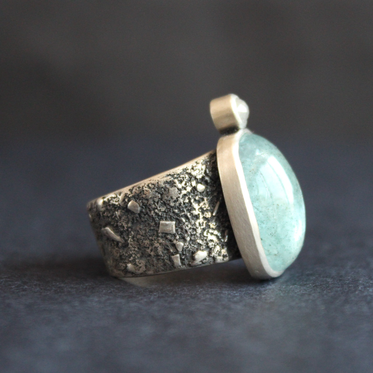 a silver ring with a pale blue aquamarine stone and smaller diamond on a textured silver band by Swedish jeweller Carin Lindberg.