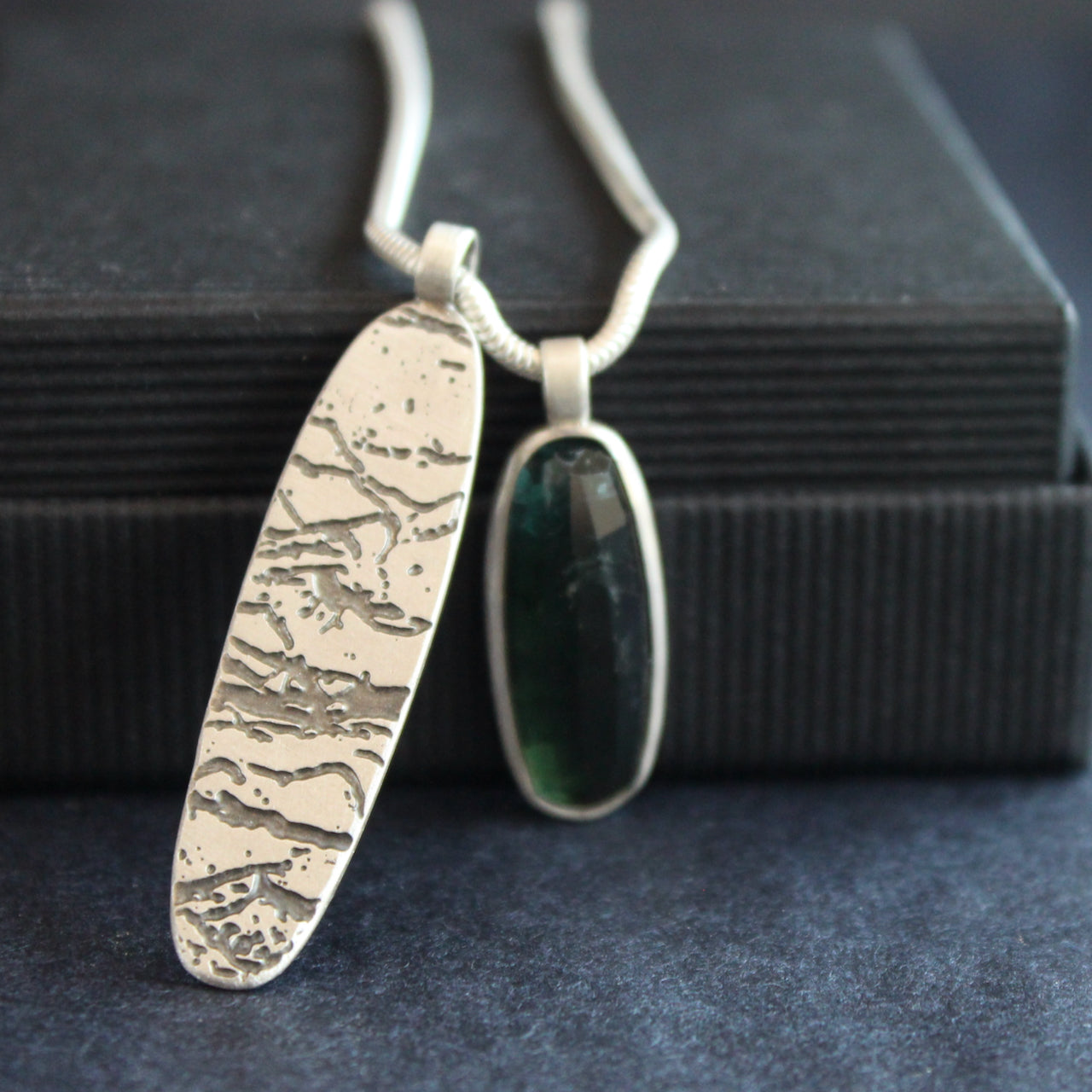 a double pendant on silver chain of blue green stone and oval shaped silver disc by jewellery designer Carin Lindberg 