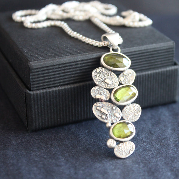 a clustered silver pendant of green stones and silver discs hanging from a silver chain by Cornwall jewellery designer Carin Lindberg