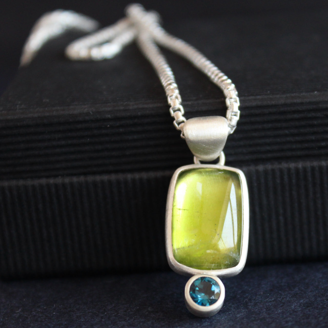 a silver pendant with a bright green stone set in silver oval and small blue stone below by Cornwall jewellery designer Carin Lindberg