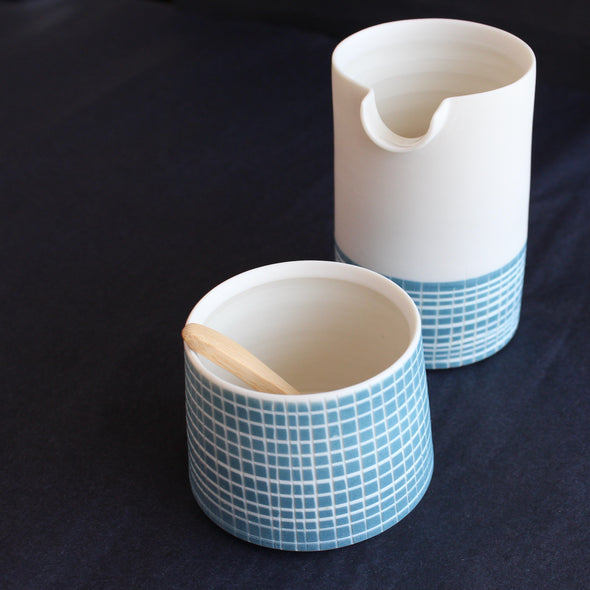 a porcelain pourer and condiment bowl set by Kathryn Sherriff of By the Line Pottery each is designed with a blue cross hatch glaze 