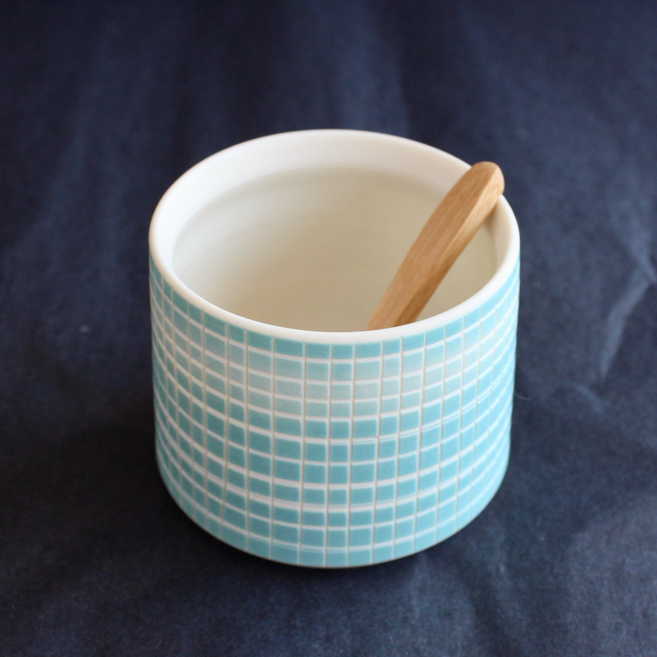 a ceramic condiment bowl with wooden spoon by Kathryn Sherriff of By the Line Pottery decorated with a blue cross hatch design which covers the whole bowl 