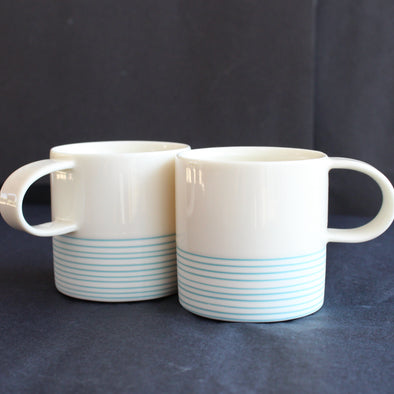 pair of small espresso style cups by Kathryn Sherriff of By the Line Pottery they are in white porcelain with a turquoise ring design around the bottom half 
