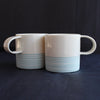 a pair of small espresso style cups by Kathryn Sherriff of By the Line Pottery they are in white porcelain with a turquoise ring design around the bottom half of each cup