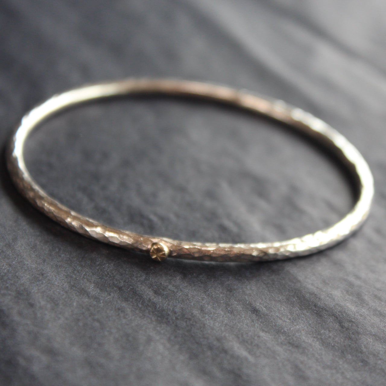 a narrow textured silver bangle with small gold dot by Cornwall jewellery designer Lucy Spink.