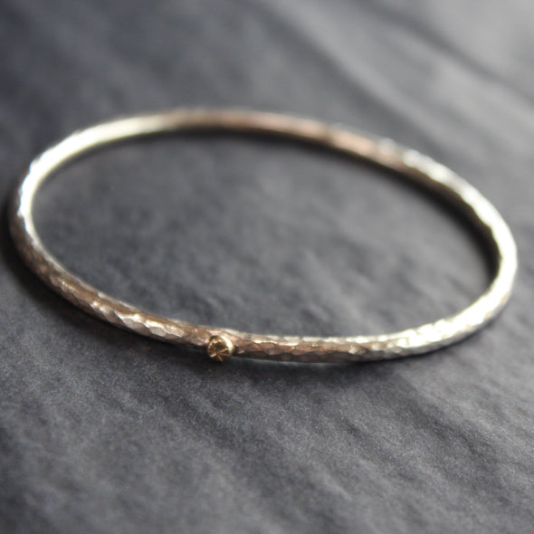 a narrow textured silver bangle with small gold dot by Cornwall jewellery designer Lucy Spink.