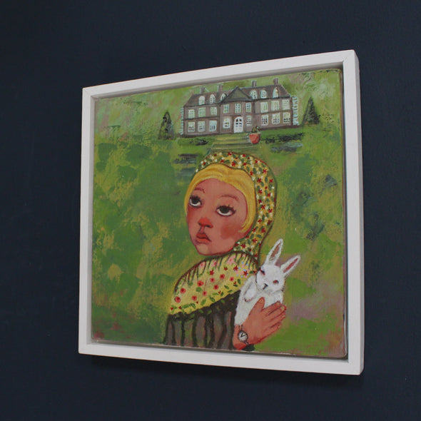 a framed painting by Cornwall artist Siobhan Purdy of a blonde haired girl holding a rabbit standing in front of a large house and garden .