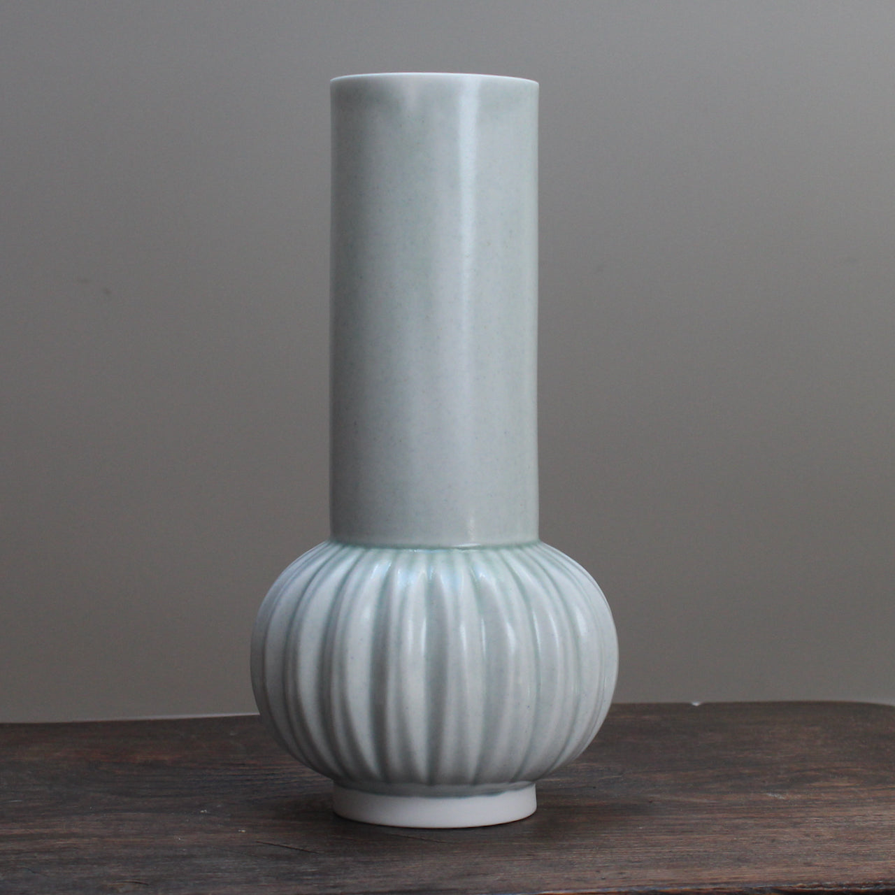 Tall pale green vase with a straight top and curved bottom on wooden table