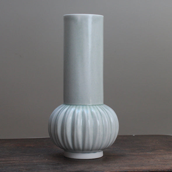 Tall pale green vase with a straight top and curved bottom on wooden table 
