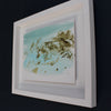 a framed pale blue, white and brown abstract Katy Brown painting of flotsam on a sandy beach