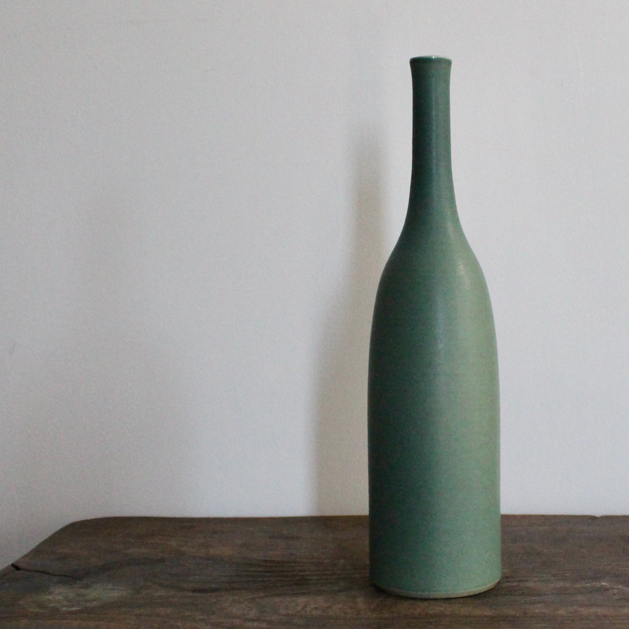 green glazed ceramic bottle on a wooden table it's by UK ceramicist Lucy Burley