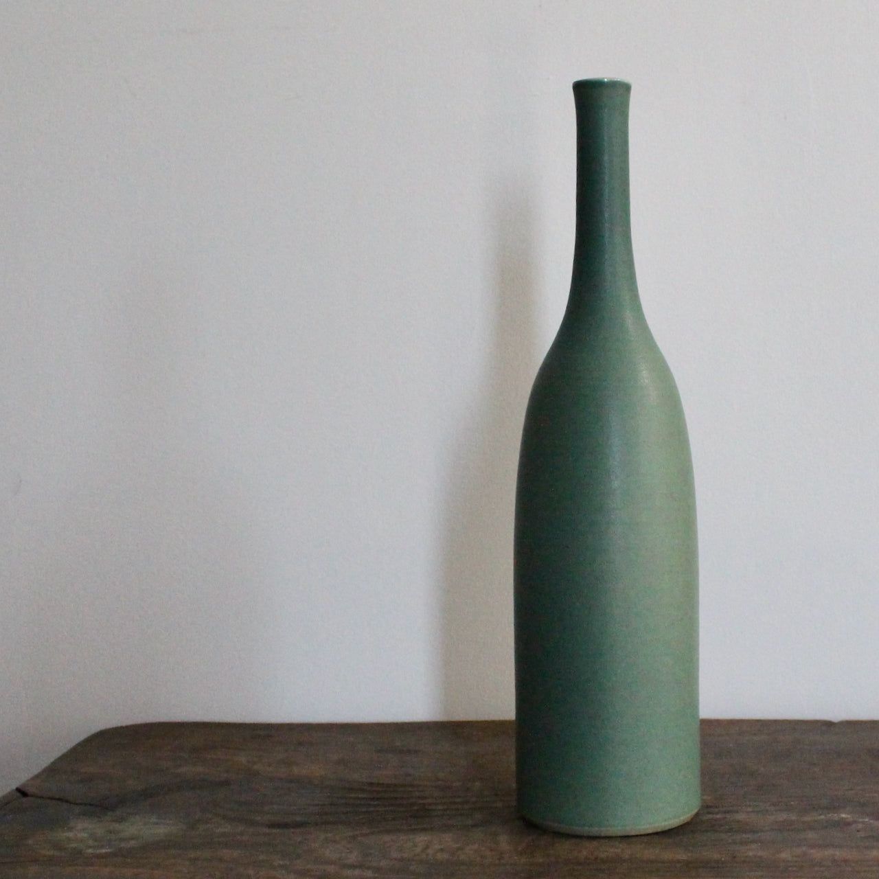 green glazed ceramic bottle on a wooden table it's by UK ceramicist Lucy Burley 