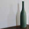 a green glazed ceramic bottle on a wooden table it's by ceramicist Lucy Burley. 