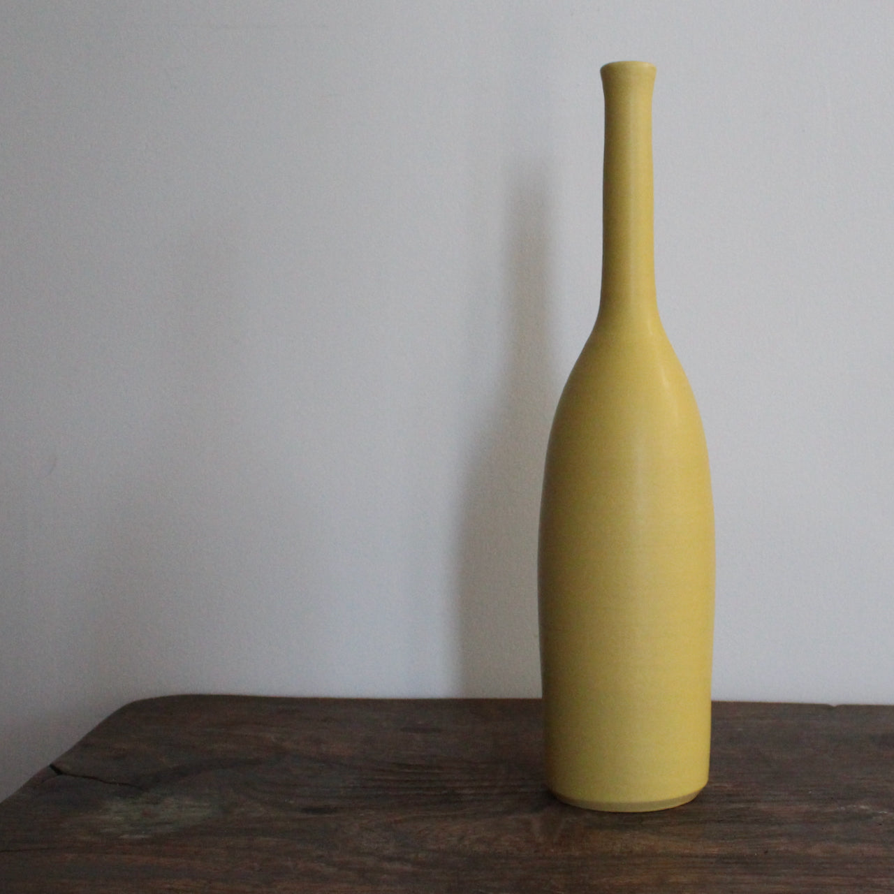 yellow ceramic bottle on a wooden table it's by UK ceramicist Lucy Burley